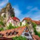 Halftimbered houses with red tiled roofs perched on a steep mountain with a large rock formation towering over the village - Tuchersfeld Bavaria
