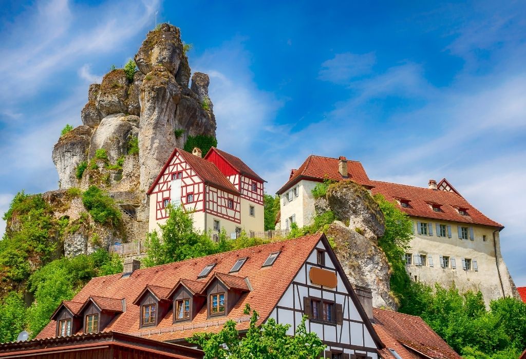 Halftimbered houses with red tiled roofs perched on a steep mountain with a large rock formation towering over the village - Tuchersfeld Bavaria